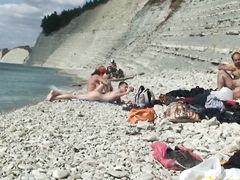 Обнаженные мужики и девочки отдыхают на каменистом пляже